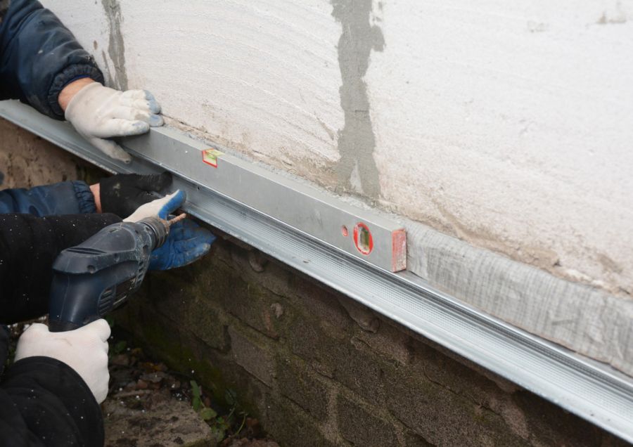 Workers installing a metal drainage trim on a building wall with a drill and level